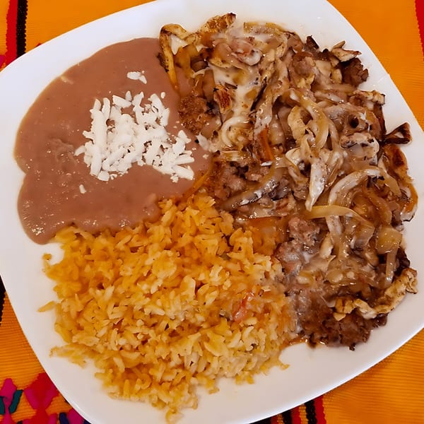 A Castañedas Mexican Restaurant plate with carne asada, refried beans topped with cheese, and rice.