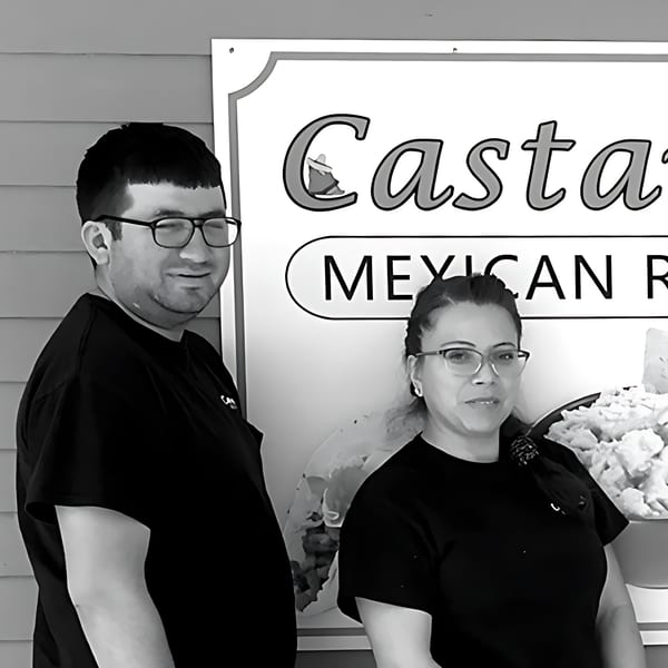 Two Castañedas Mexican Restaurant employees, a man and a woman, smiling next to the restaurant sign.