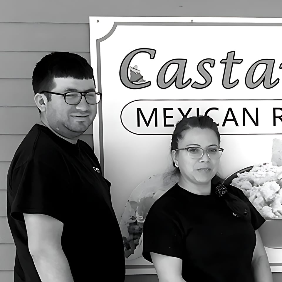 Two Castañedas Mexican Restaurant employees, a man and a woman, smiling next to the restaurant sign.