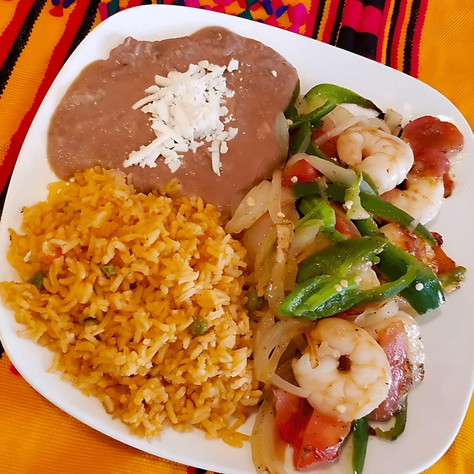 A Castañedas Mexican Restaurant plate with shrimp fajitas, rice, and refried beans topped with cheese.
