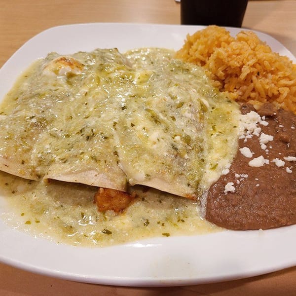 Two enchiladas verdes covered in green sauce and cheese, with a side of rice and refried beans.