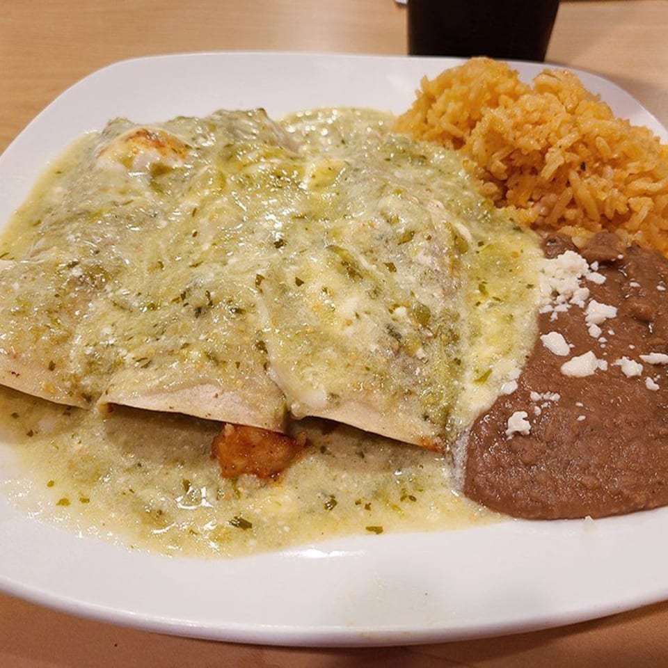 Two enchiladas verdes covered in green sauce and cheese, with a side of rice and refried beans.