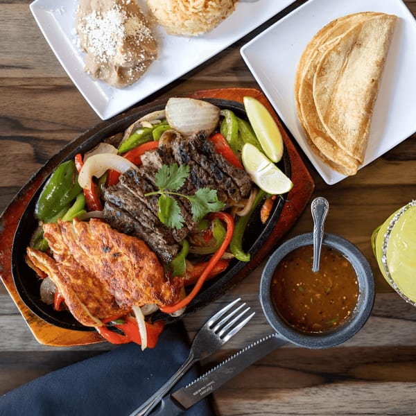 Sizzling Castañedas Mexican Restaurant fajitas with steak, chicken, peppers, onions, rice, beans, tortillas, and salsa.