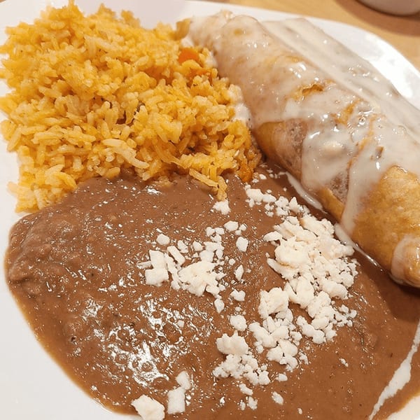 A Castañedas Mexican Restaurant plate with a burrito covered in white sauce, rice, and refried beans with cheese.