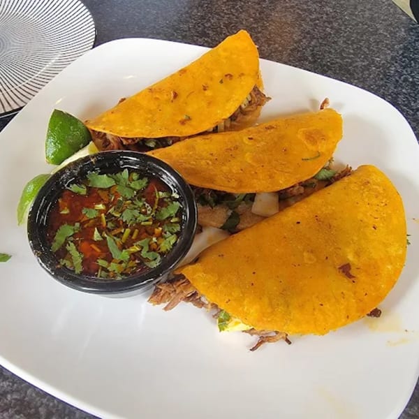 Three Castañedas Mexican Restaurant birria tacos with a side of consommé and lime wedges.