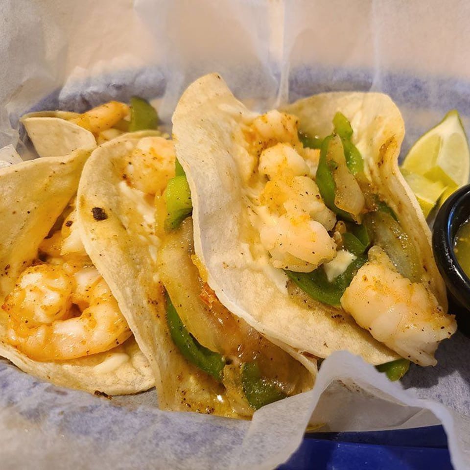 Three Castañedas Mexican Restaurant shrimp tacos with peppers, onions, and lime wedges in a basket.