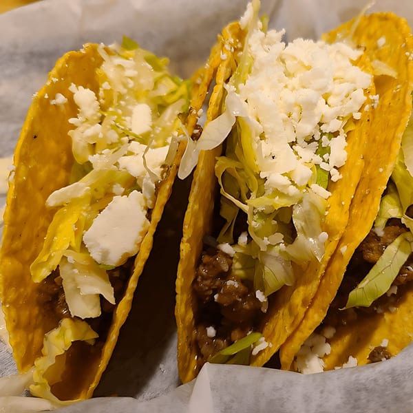 Three Castañedas Mexican Restaurant tacos with ground beef, shredded lettuce, and crumbled white cheese.