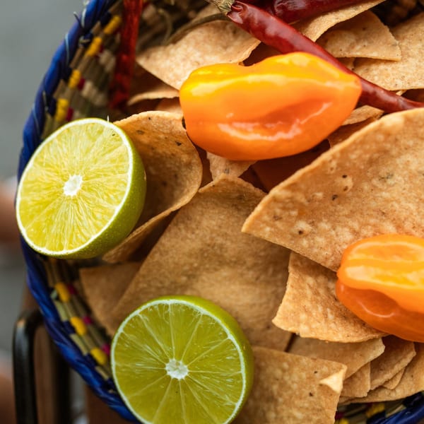 Close-up of tortilla chips in a colorful basket with lime halves and orange and red peppers.