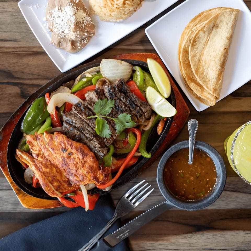 Sizzling Castañedas Mexican Restaurant fajitas with steak, chicken, peppers, onions, rice, beans, tortillas, and salsa.