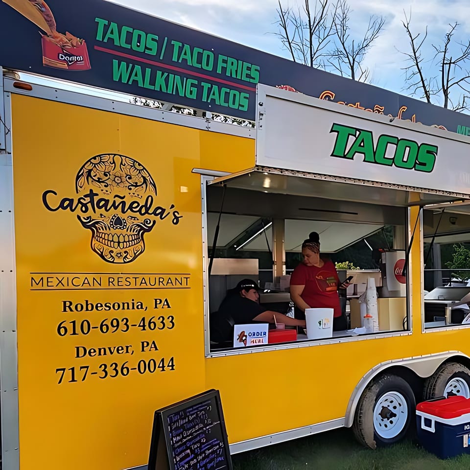 Castañeda's Mexican Restaurant food truck, yellow with a sugar skull logo, serving customers.