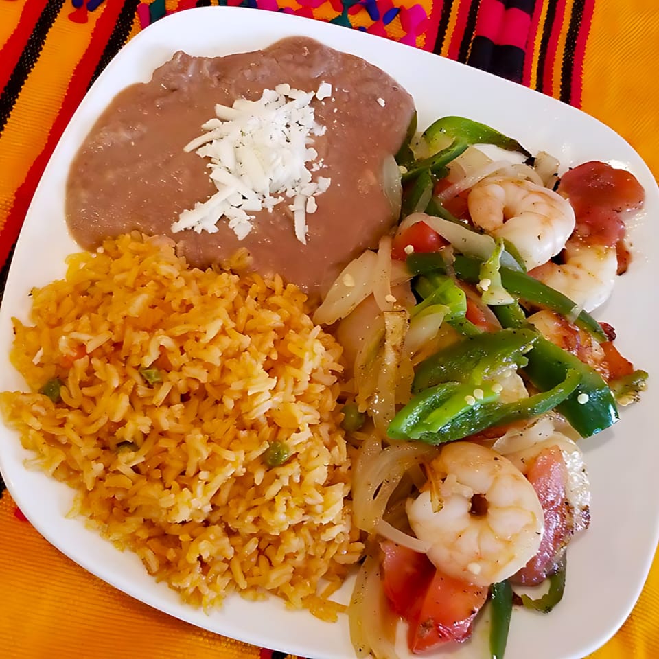 A white plate with Castañedas Mexican Restaurant's shrimp fajitas, rice, and refried beans with cheese.