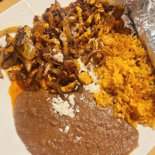 Mexican dish with seasoned chicken and onions, yellow rice, and refried beans with cheese.