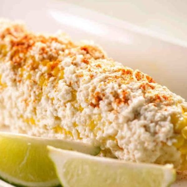 Elote, Mexican street corn, covered in white cheese and chili powder, with lime wedges.