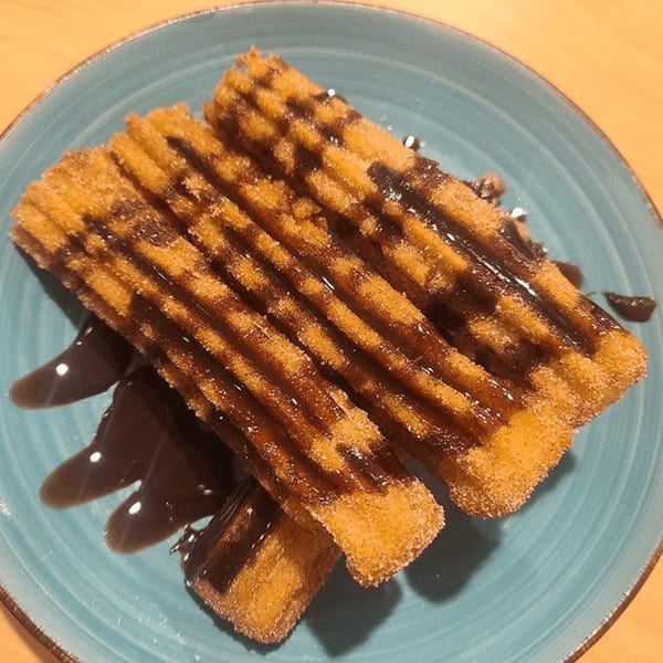 Golden-brown churros drizzled with chocolate sauce, served on a blue plate at Castañedas Mexican Restaurant.