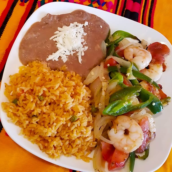 A plate of Castañedas Mexican Restaurant's shrimp fajitas with rice and refried beans, garnished with cheese.